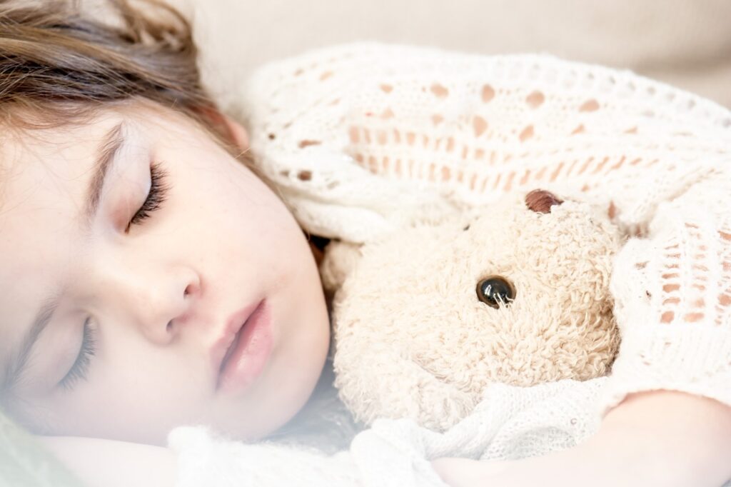 クマのぬいぐるみを抱いて眠る少女